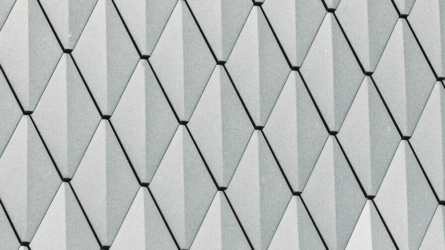 Trapézová vikýřová střecha rodinného domu v Mechernichu, obložená malými falcovanými šablonami PREFA v barvě P.10 antracitová. Střecha je pokryta falcovanými šindeli PREFA DS.19 ve stejné barvě. Vysoce kvalitní hliníkové obložení zajišťuje odolnost proti povětrnostním vlivům a moderní, estetický vzhled.