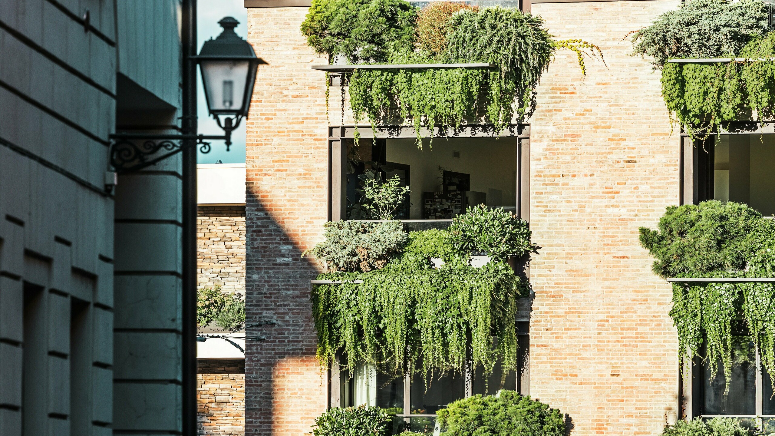 Detailní pohled na fasádu ze zelených cihel v Itálii s visutými zahradami, architektonickými detaily z odolné drážkované krytiny PREFALZ a přilehlým okolím starého města s lucernou.