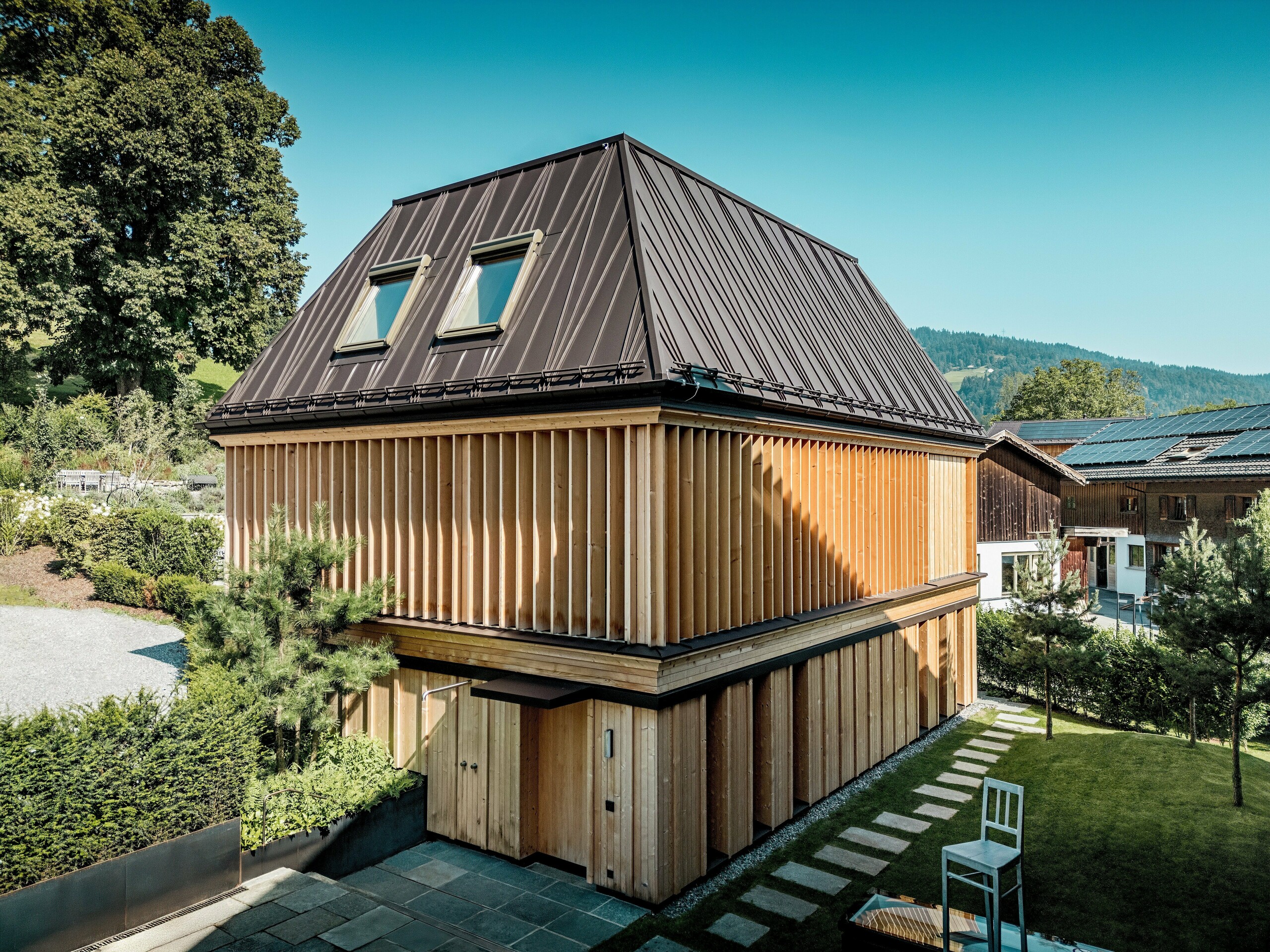 „Lázně“ hotelu Hirschen ve Schwarzenbergu se koupou v čistém, přirozeném světle. Ústředním bodem je výjimečná drážkovaná střecha PREFA v ořechově hnědé barvě P.10 s precizním zpracováním a výraznými, částečně diagonálně probíhajícími drážkami. Přirozené světlo uvnitř zajišťují dvě střešní okna. Fasáda se vyznačuje svisle uspořádanými dřevěnými lamelami od podlahy až ke stropu, které jsou esteticky i funkční. V popředí vedou desky z přírodního kamene udržovanou zahradou. Moderní budova, obklopená tradičními dřevěnými domy a zvlněnými kopci, harmonicky zapadá do krajiny Bregenzerwaldu.