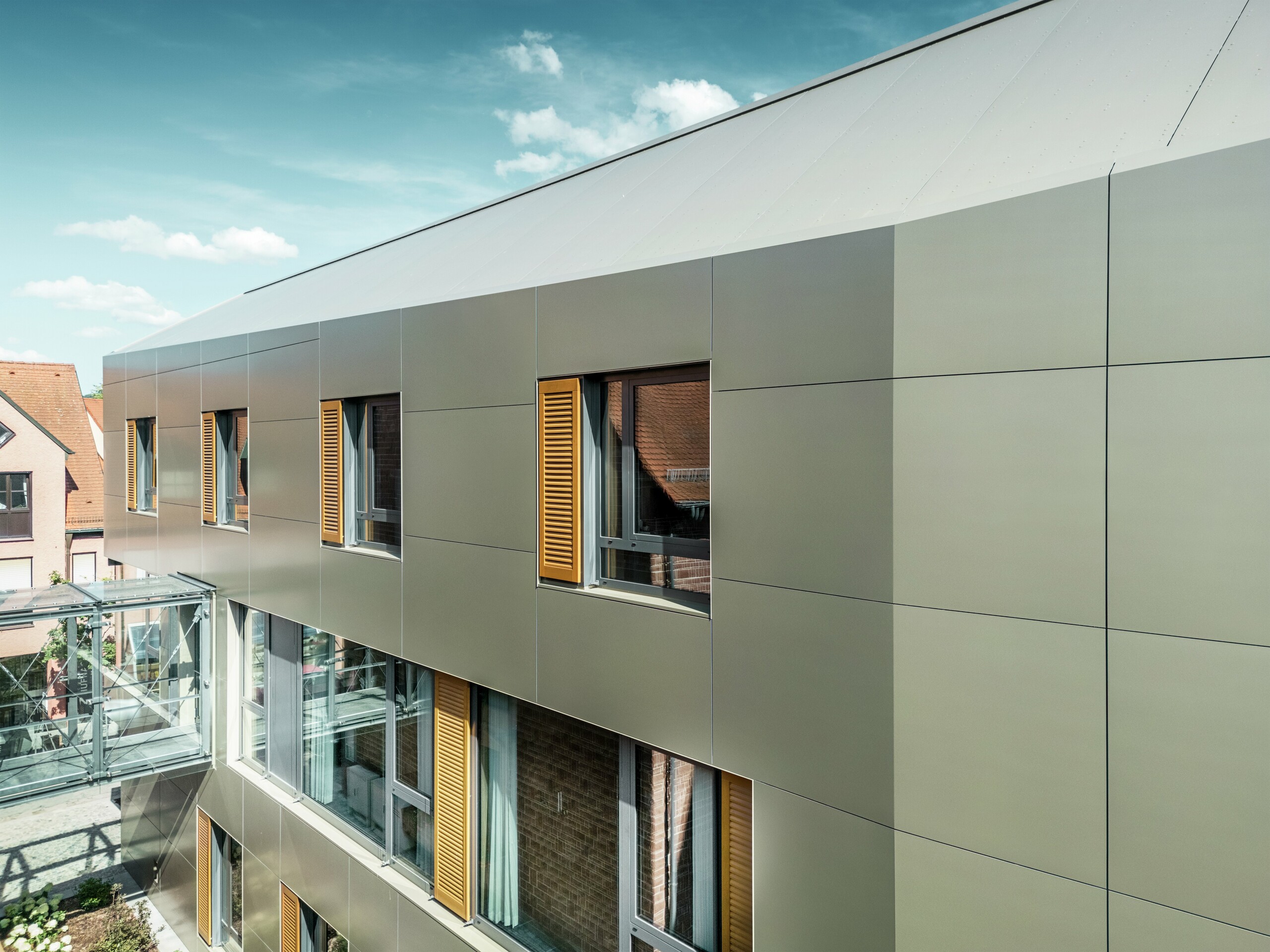 Obrázek ukazuje část fasády radnice v Alzenau v Německu s bronzovými hliníkovými kompozitními panely PREFABOND. Panely jsou položeny v moderním obdélníkovém vzoru.