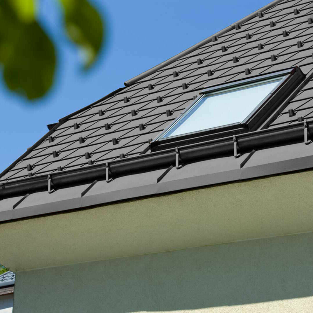 Referenční fotografie nástřešního žlabu PREFA s oknem do střechy a černou střechou.