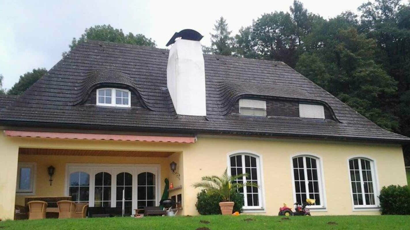 Střecha domu s velkým komínem a chmelovým vikýřem před sanací za použití PREFA falcovaných střešních šindelů 