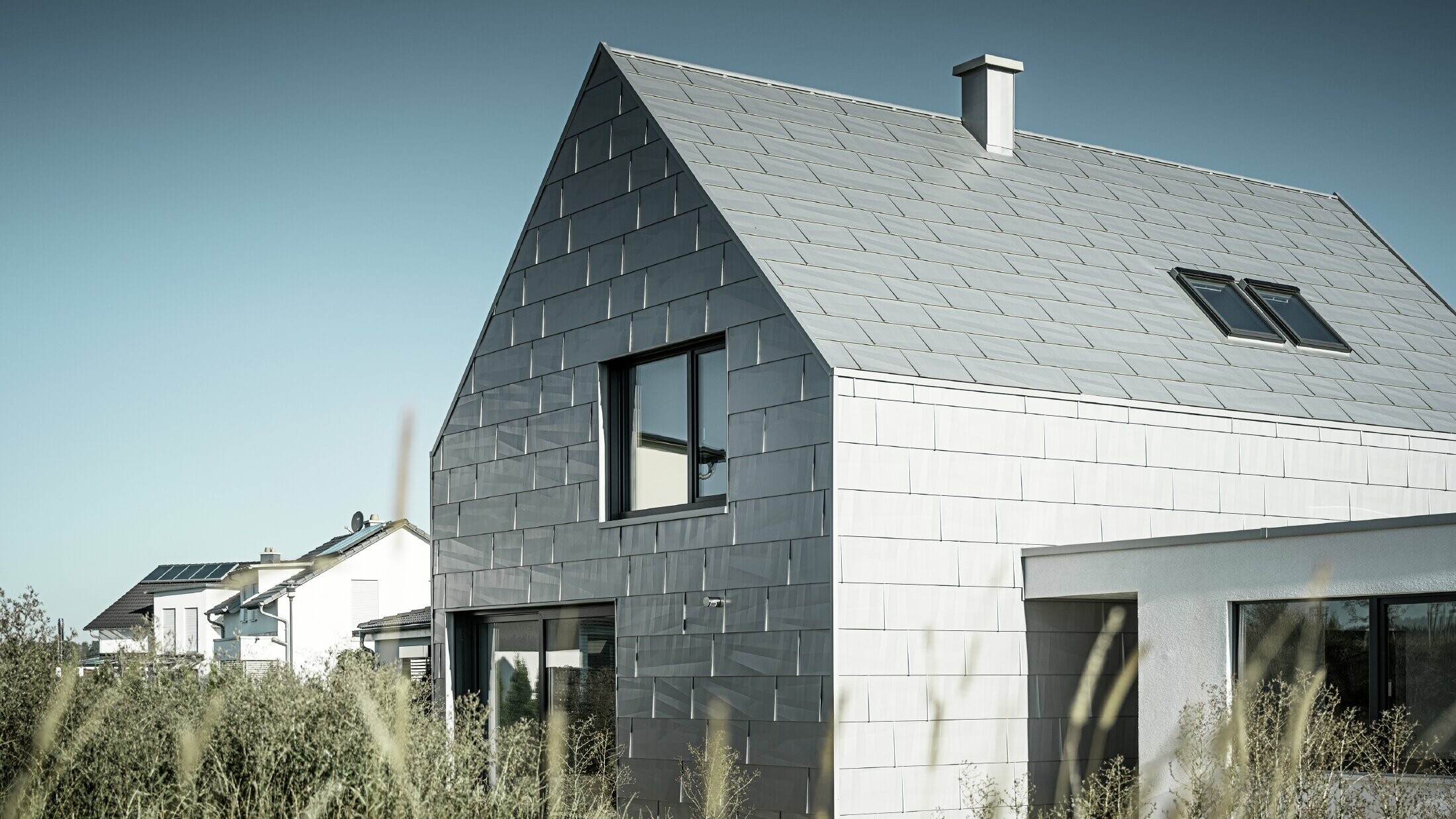 Boční pohled na kancelářskou budovu, která je kompletně pokryta PREFA střešním a fasádním panelem FX.12 v barvě P.10 stříbrná metalíza. 