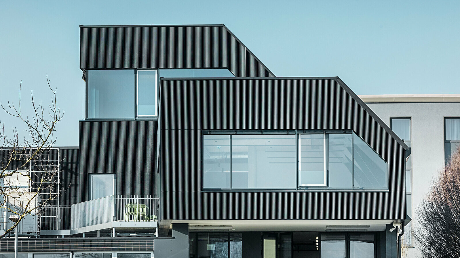 Boční pohled na kavárnu Amann za slunného dne. K ochraně budovy byl použit černý lisovaný profil Zackenprofil.