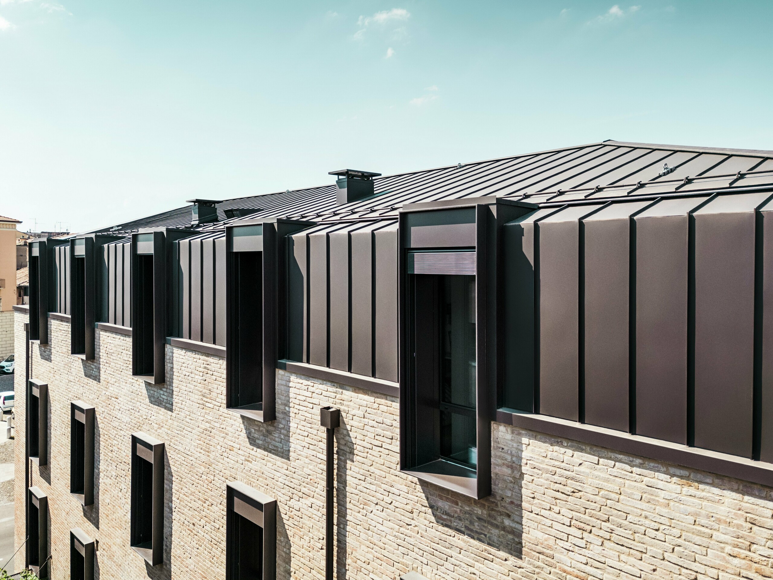 Moderní návrh střechy a fasády cihlového domu v Itálii s hliníkovou střechou z PREFALZ v barvě P.10 oříškové a výraznými střešními okny