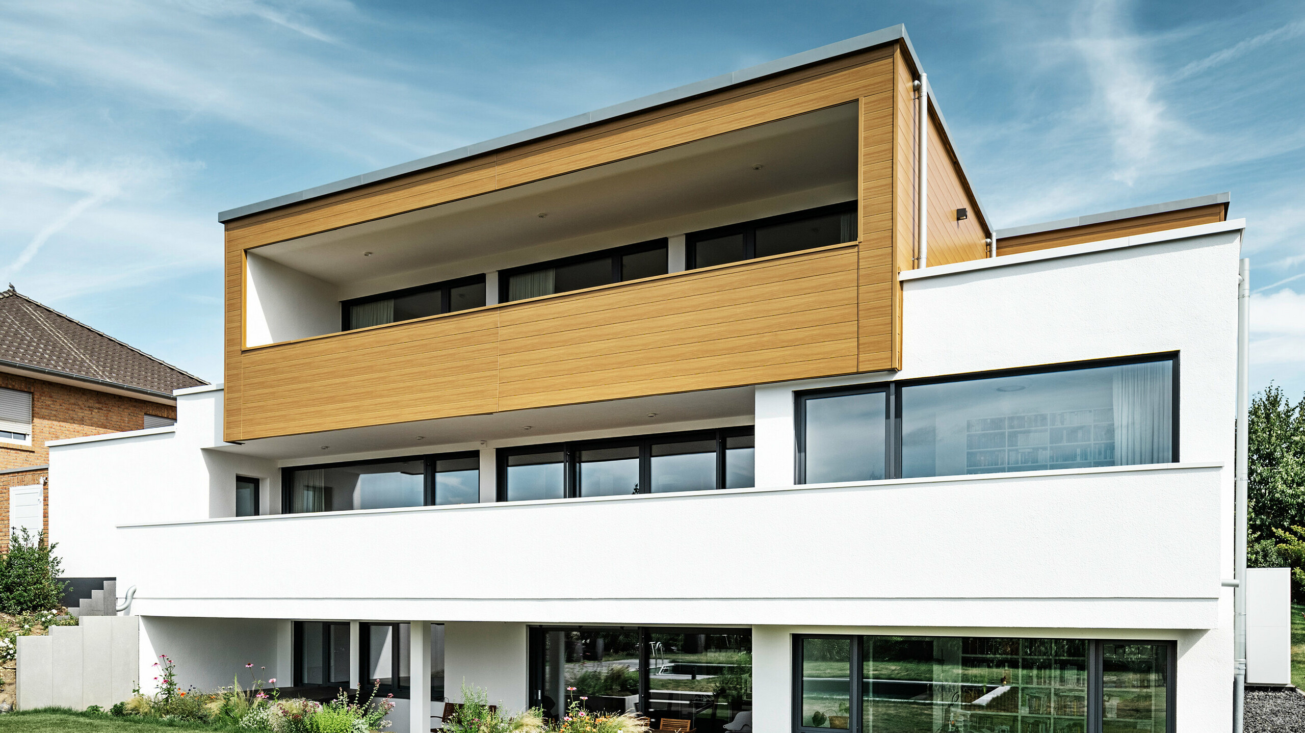 Pohled na zahradu a rodinný patrový dům s kombinovanou fasádou - přízemí bílá omítková a horní parto s hliníkovou fasádou v optice dřeva