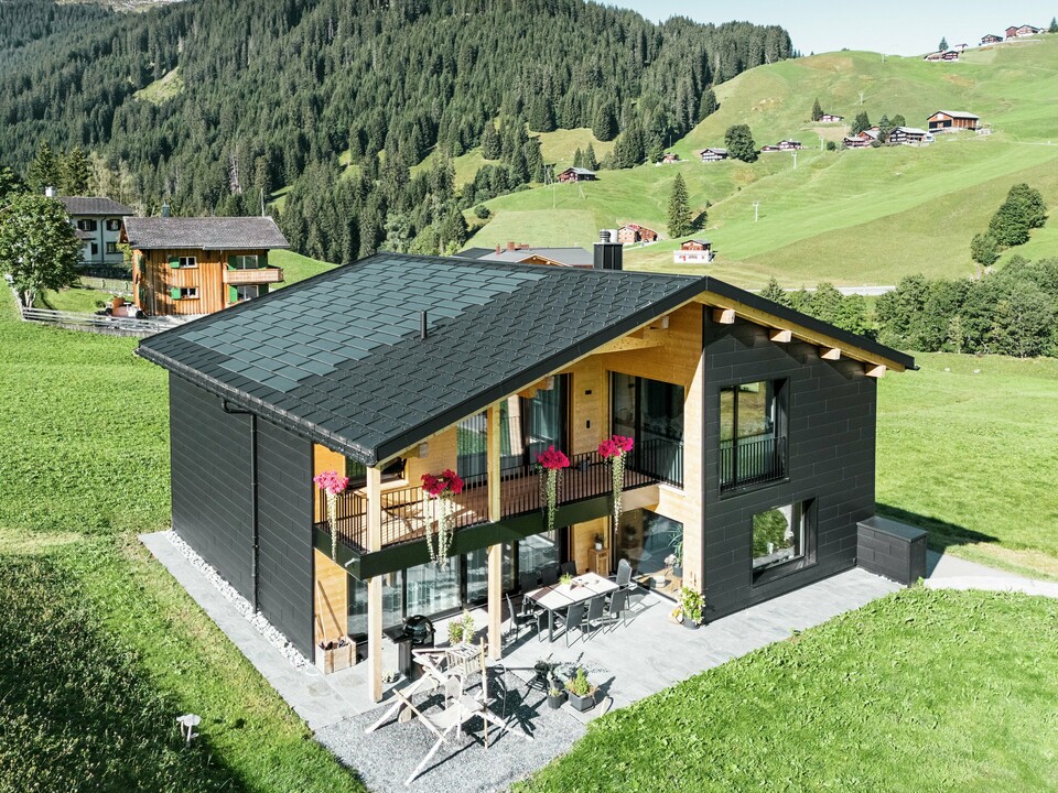 Das elegante Einfamilienhaus in der hügeligen Umgebung von Ascharina (Schweiz) zeigt, wie sich Aluminium und Holz perfekt kombinieren lassen. Die robusten PREFA Siding.X Fassadenpaneele in P.10 Schwarz harmonieren mit dem Dach aus PREFA Solardachplatten und Dachplatten R.16 in der gleichen Farbbeschichtung. Die langlebige Aluminiumhülle schützt das Gebäude zuverlässig vor den Herausforderungen des alpinen Klimas.