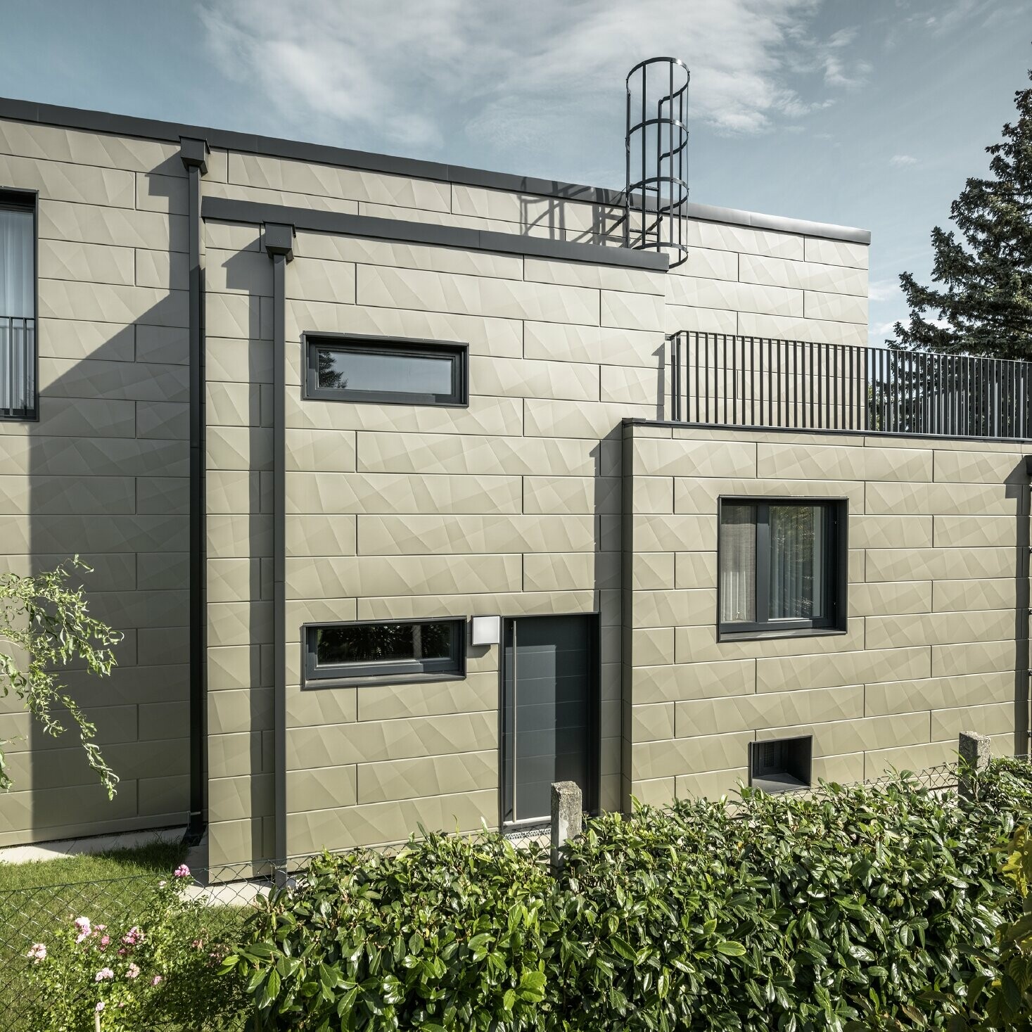 Novostavba s plochou střechou, fasáda je obložena fasádními lamelami PREFA Siding.X se zlomy v bronzové barvě, lemováním a hranatým žlabem i svodem v antracitové barvě,   