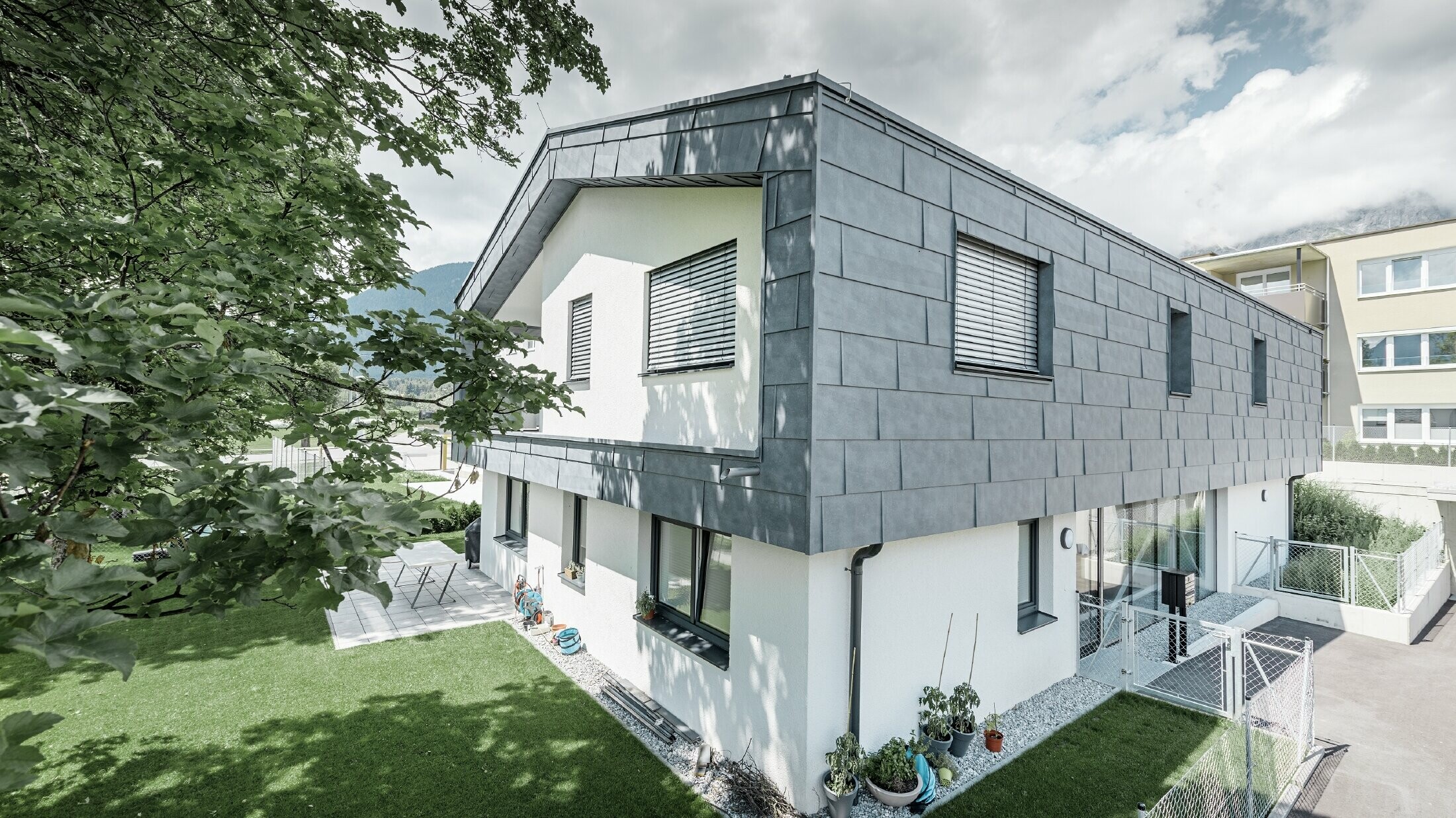 Moderní nástavba obytného domu s plochou sedlovou střechou bez přesahu; fasádní obklad byl proveden pomocí fasádních panelů PREFA FX.12 v barvě břidlicová.