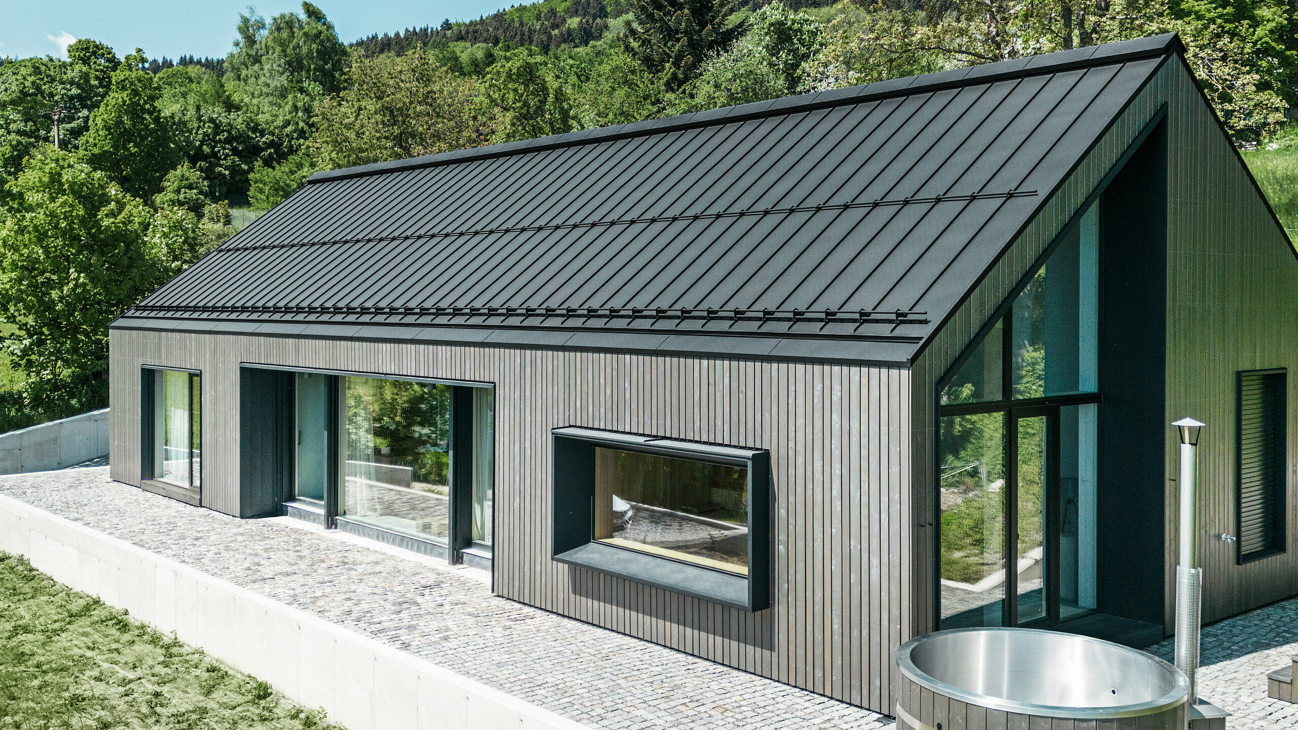 Moderní dřevostavba z masivního dřeva se střechou z PREFALZ v barvě P.10 černé. Střecha má zaatikové žlaby a nemá přesah. Na obrázku také wellness koutek.