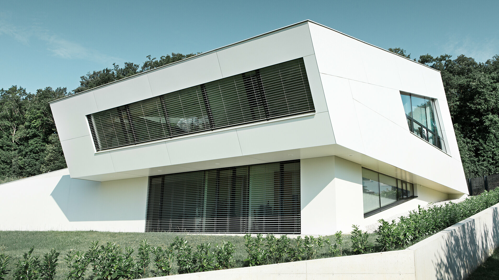 Velmi moderní rodinný dům opláštěný kompozitními deskami v čiště bílé barvě a velkým prosklenými plochami