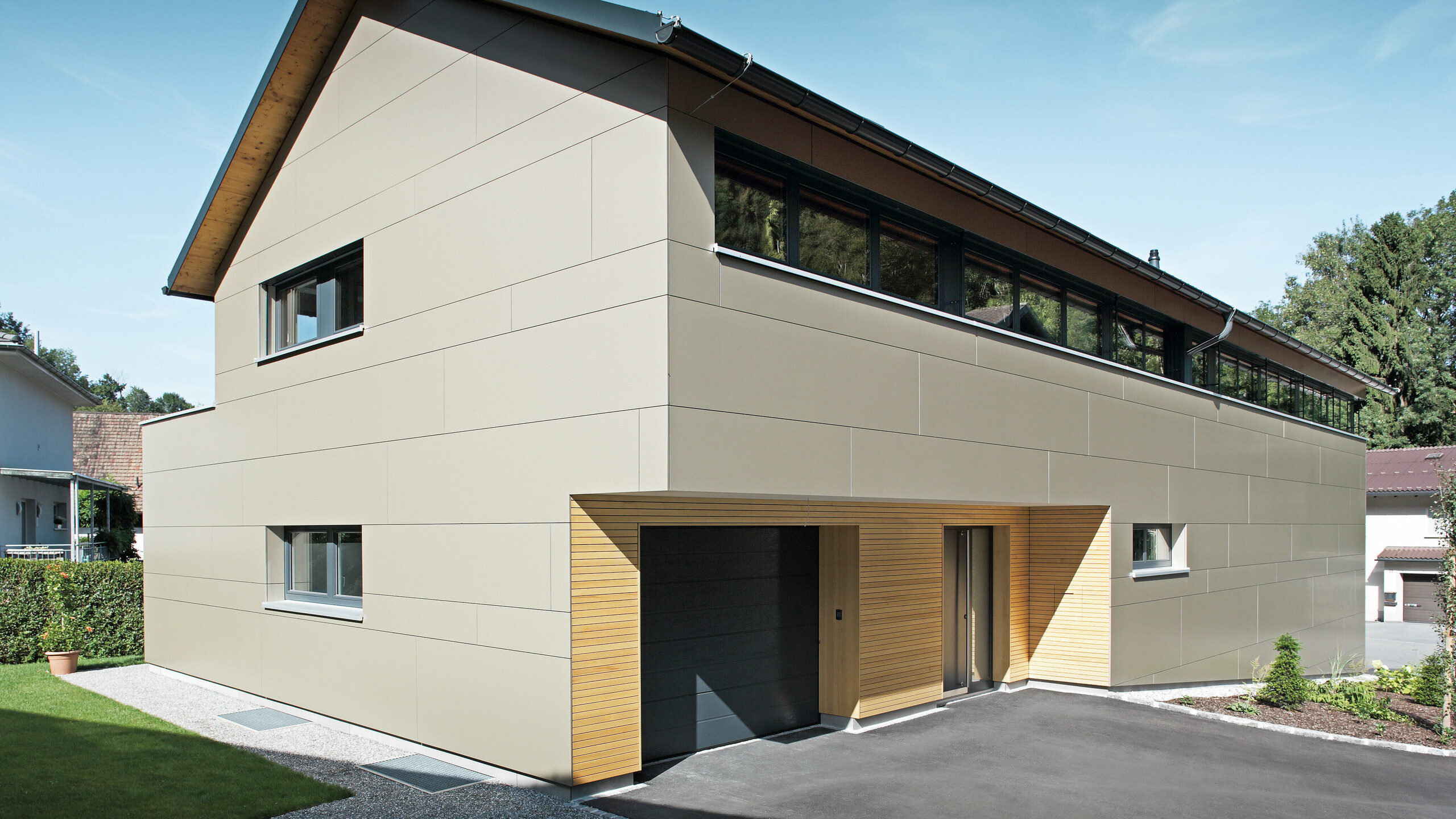 Elegantes Einfamilienhaus in Hohenems, ausgestattet mit einem PREFA Komplettsystem. Die Fassade besteht aus Aluminium Verbundplatten in Bronzemetallic, die einen modernen und klaren Look schaffen, während die Holzelemente am Garageneingang Wärme und Natürlichkeit ausstrahlen. Das Dach ist mit PREFA Dachplatten in P.10 Anthrazit gedeckt, die zusammen mit der Fassade ein architektonisches Gesamtkonzept bilden und das Haus effektiv schützen.