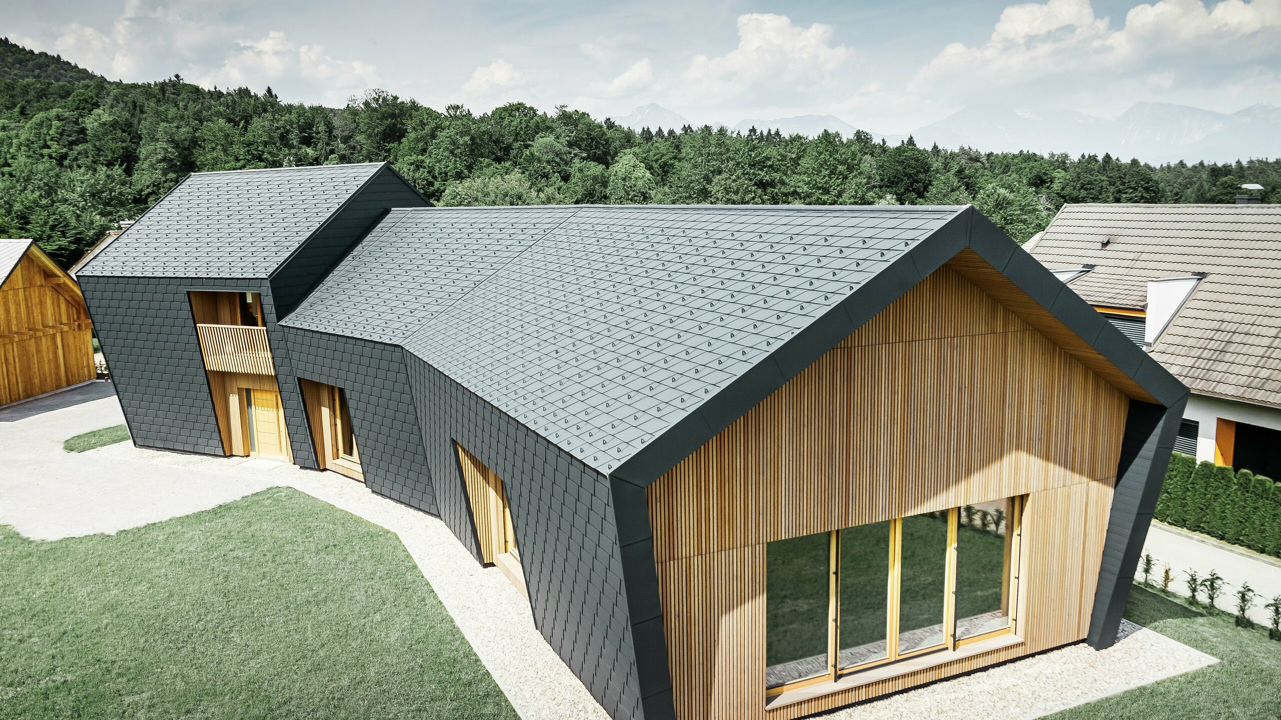 Velké střešní a fasádní plochy, pokryté falcovaným šindelem DS.19 v barvě P.10 antracitová, na čelní straně je fasáda obložená dřevem