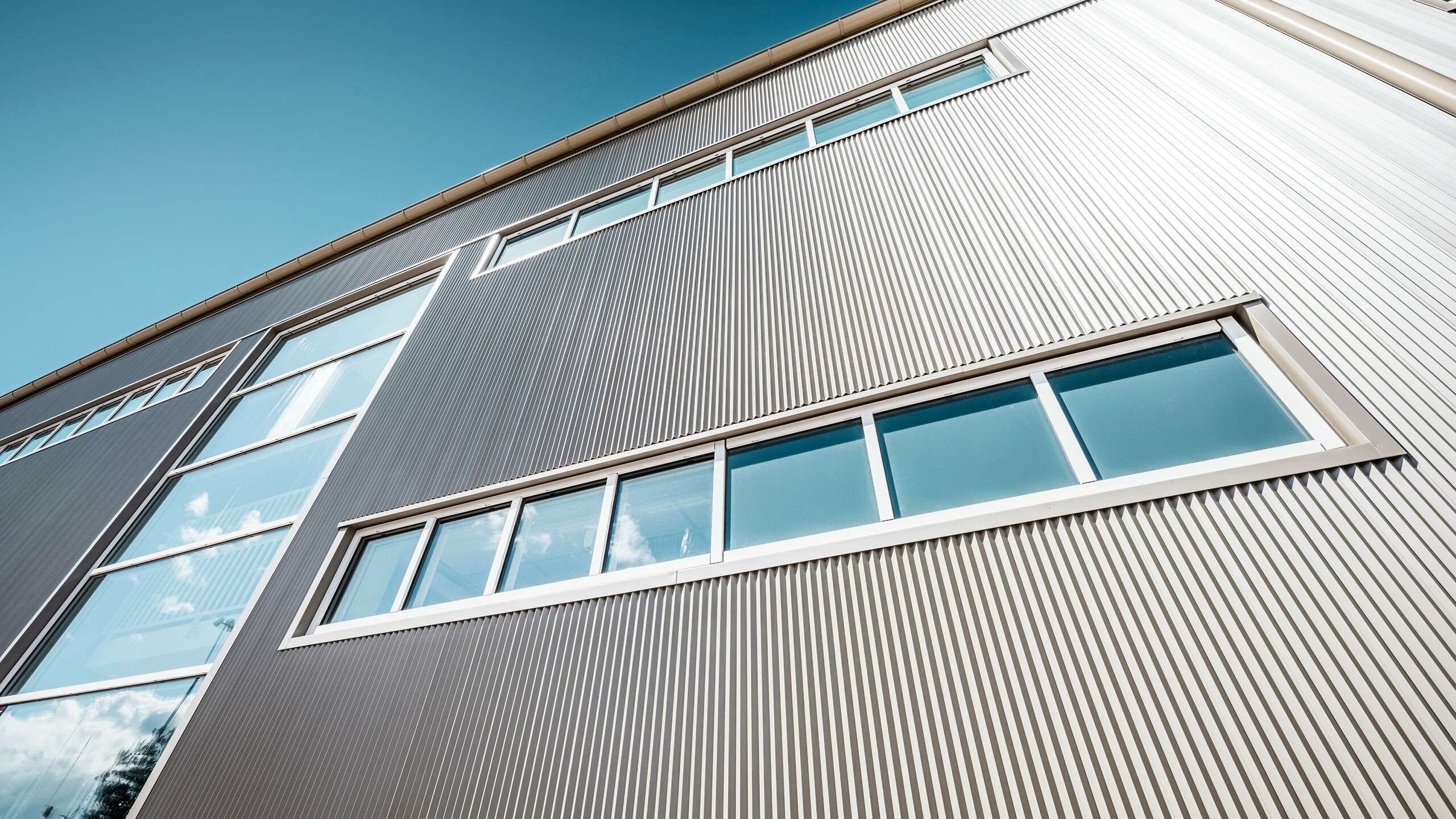 Vnější pohled na Park Arena ve Värnamo, Švédsko s moderní hliníkovou fasádou PREFA v bronzu. Lisované pilové Zackenprofily vytvářejí výrazné světelné a stínové efekty. Vsazená okna harmonicky zapadají do precizně zpracované fasády, která je zárukou dlouhé životnosti, odolnosti a současného designu.