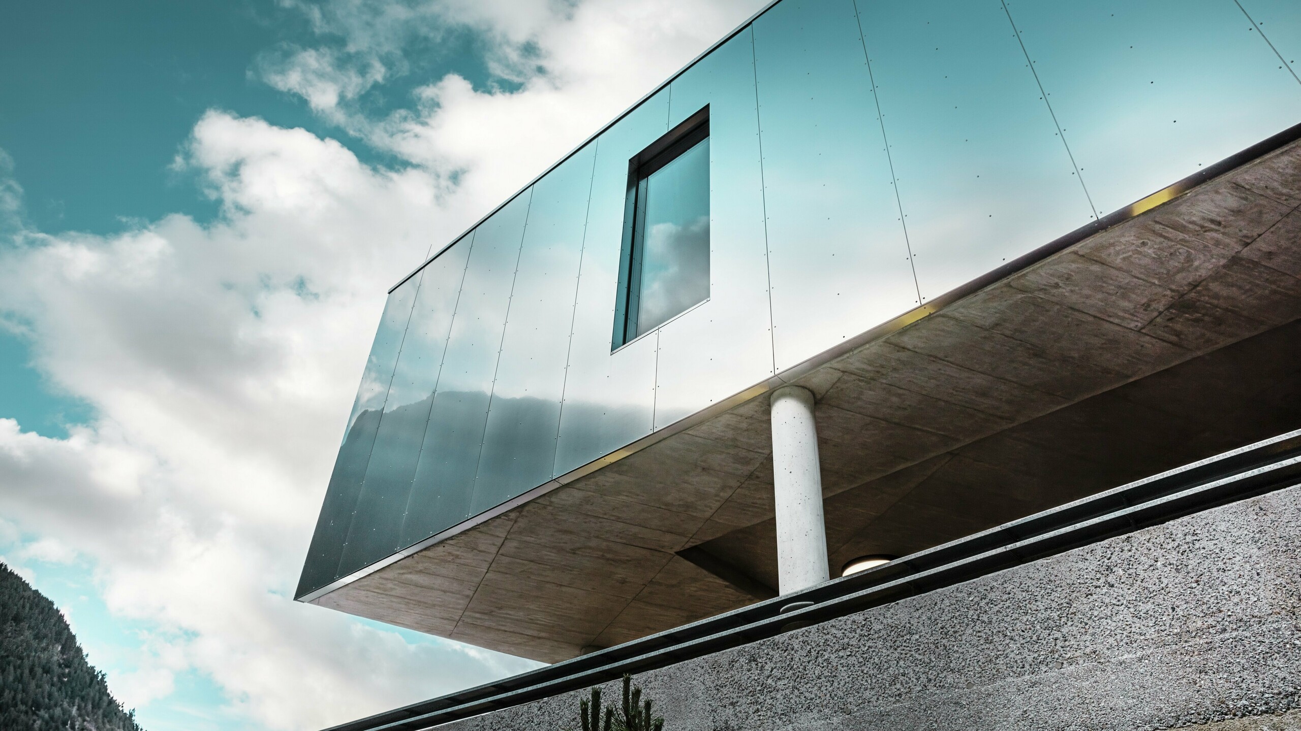 Moderne Architektur des MPREIS Supermarktes in Sölden, Tirol, mit reflektierenden PREFA Aluminium Verbundplatten in der Sonderfarbe Reflective Natural. Die glänzende Fassade spiegelt den Himmel und die Berglandschaft wider. Klare Linien und massive Betonsäulen verbinden innovatives Design mit Stabilität und Eleganz.