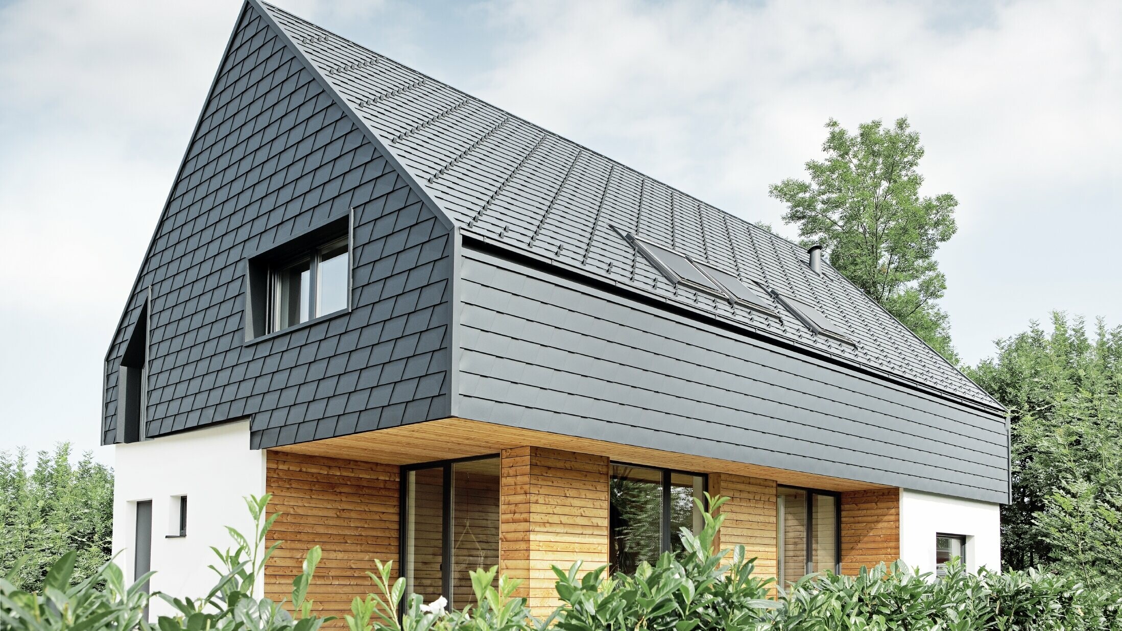 Rodinný domek se sedlovou střechou, pokrytý PREFA šindelem v barvě P.10 antracitové; šindele jsou použity také na fasádě v horním podlaží a na štítu