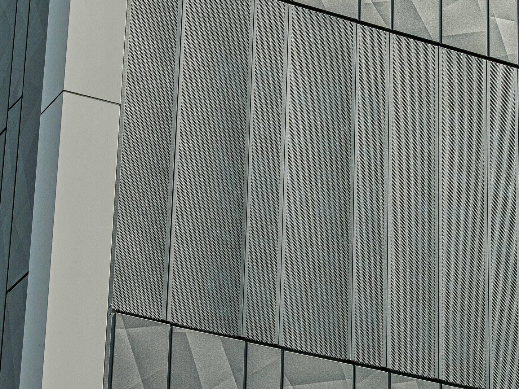 Pohled na fasádu obchodu Eurospar v Rohrbachu s obkladem PREFA Siding.X a perforovanými obklady v antracitové barvě. Prvky Siding.X vytvářejí živý geometrický vzor spár, zatímco perforované obklady nabízejí moderní strukturu propouštějící vzduch.