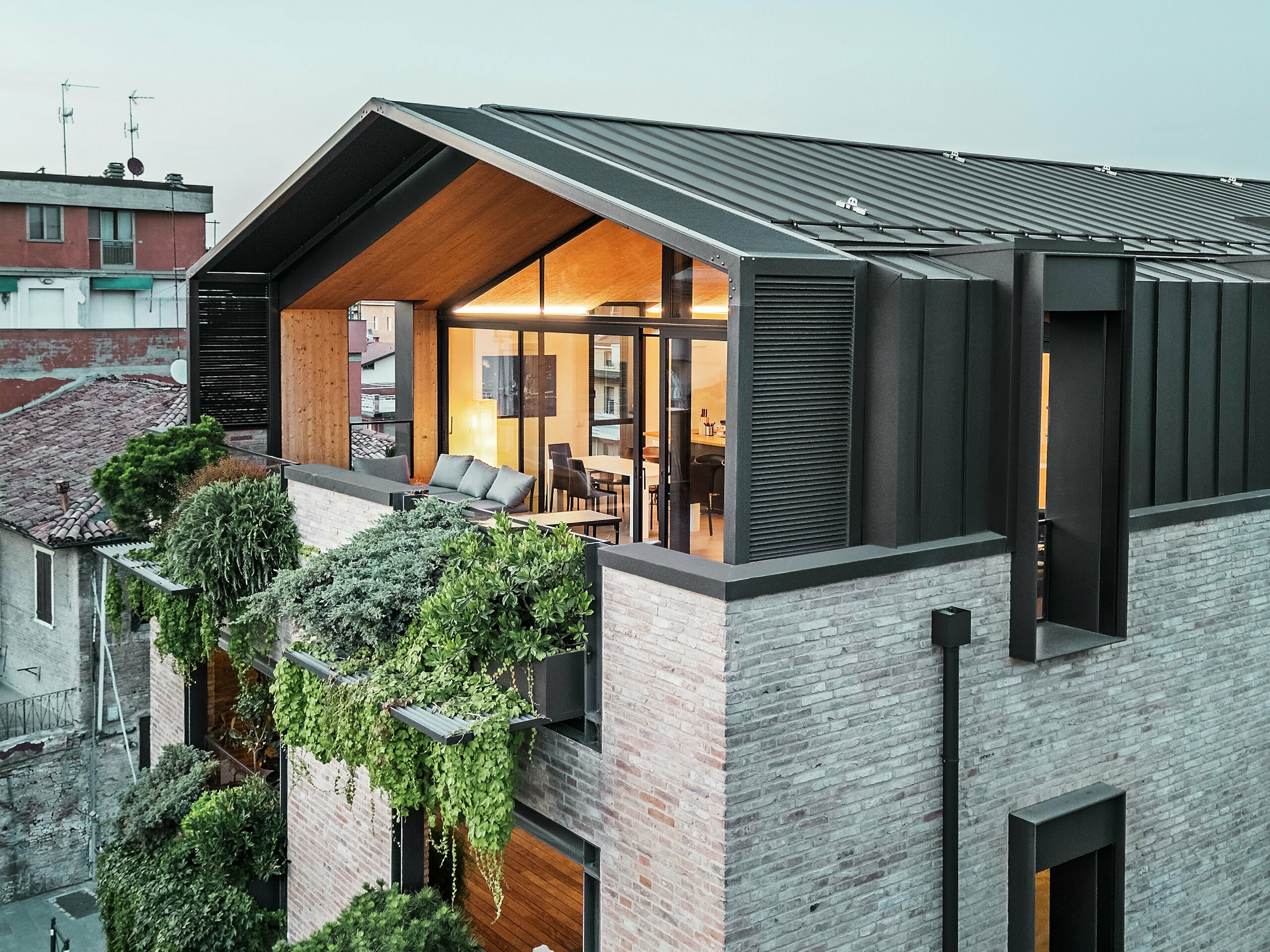Moderní obytný dům v Itálii s hliníkovou střechou z drážkované krytiny PREFALZ v ořechově hnědé barvě P.10, velkými prosklenými plochami, zelenou fasádou a cihlovou konstrukcí – zdařilá kombinace udržitelnosti a současné architektury