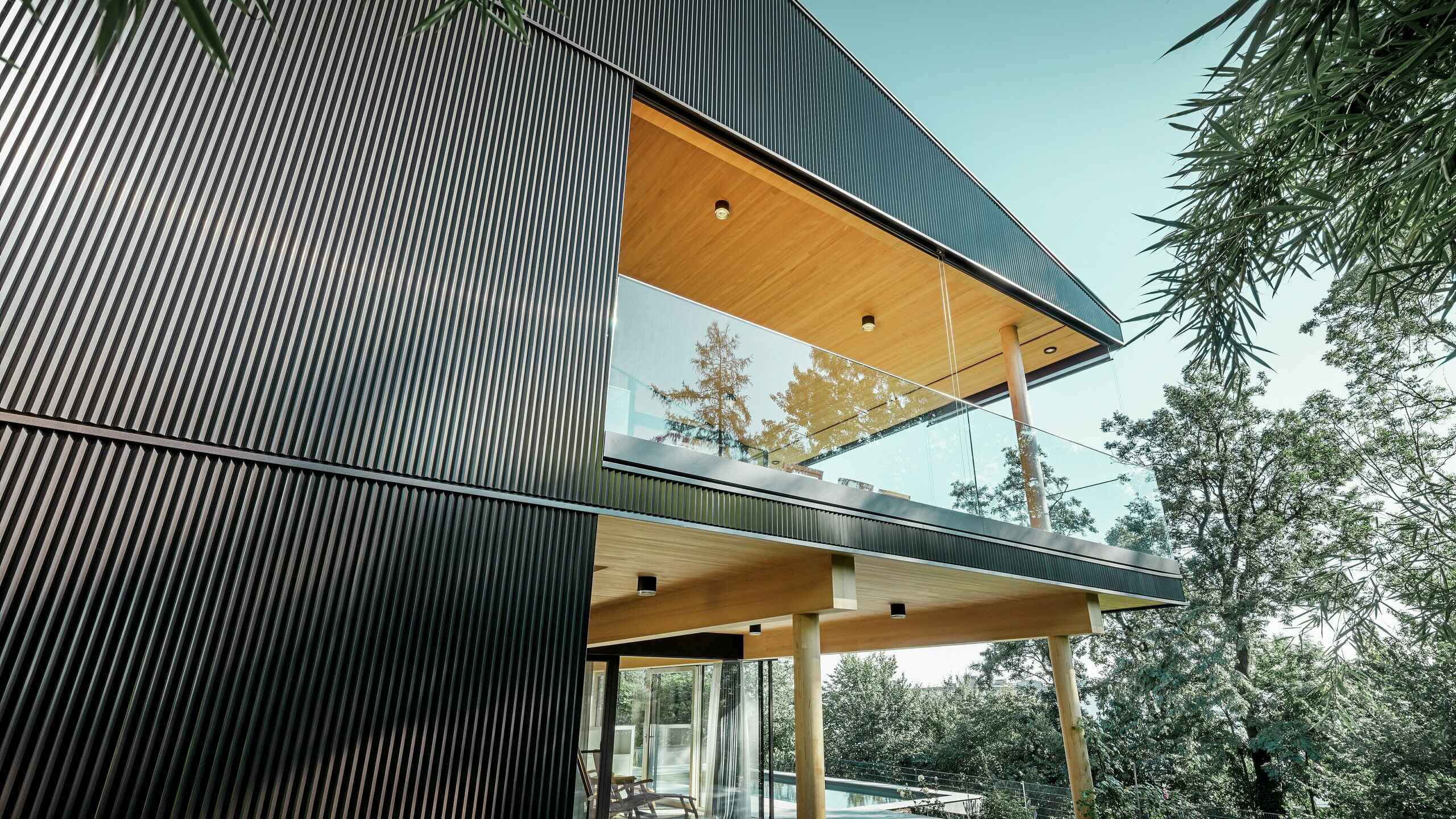 Boční pohled na rodinný dům, fasáda je obložena tmavým pilovým Zackenprofilem PREFA. Dále lze vidět terasu a prostorný balkon. Strop a podhledy jsou obloženy  dřevěnými panely.