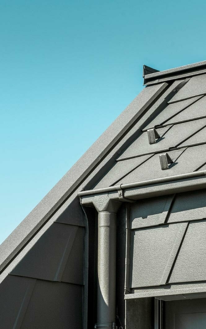 Dach mit PREFA Aluminiumdachplatten und modernen Regenrinnen, die eine hohe Langlebigkeit und ästhetische Funktionalität bieten, vor einem klaren blauen Himmel.