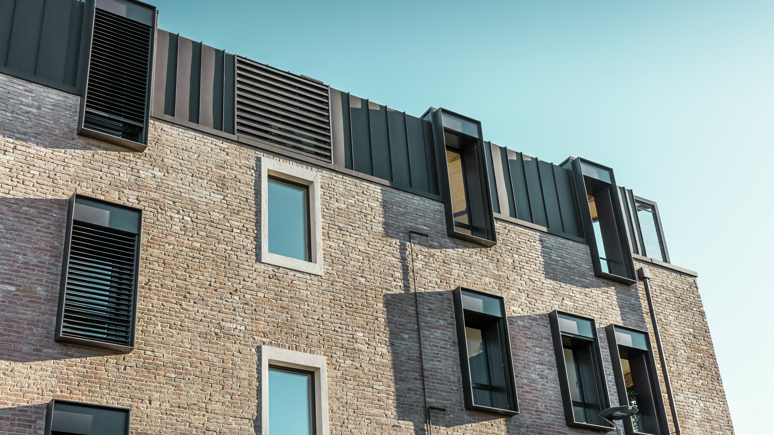 Detailní pohled na zrekonstruovaný cihlový dům v Itálii s hliníkovou střechou z drážkované krytiny PREFALZ v ořechově hnědé barvě P.10 a moderními vikýři – zdařilá kombinace tradiční cihlové konstrukce a současné architektury