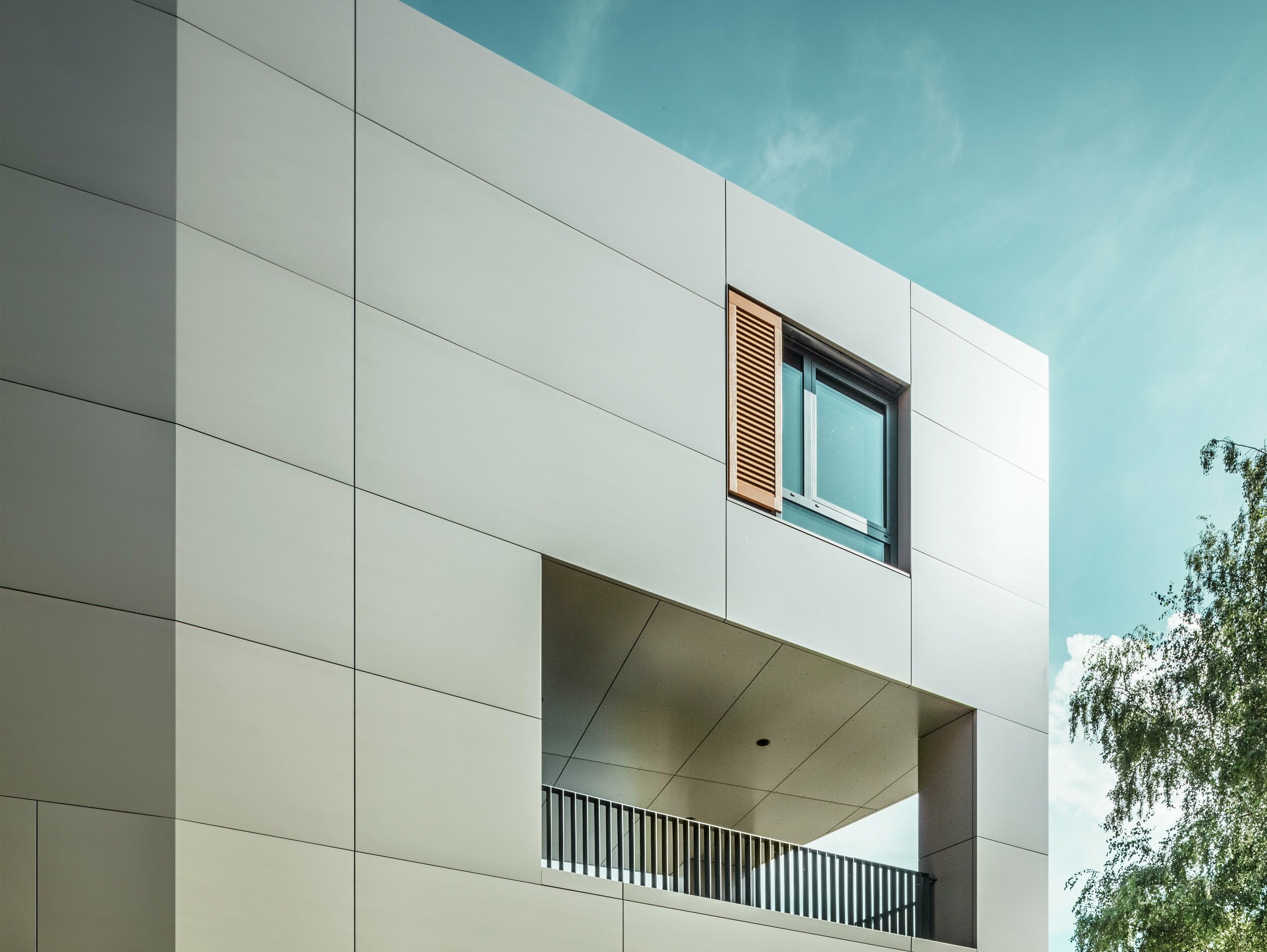 Obrázek ukazuje moderní radnici v Alzenau s fasádou z bronzových hliníkových kompozitních panelů od společnosti PREFA. Architektura se vyznačuje jasnými geometrickými tvary a velkými okny. Špičatá střecha a decentní osvětlení dodávají budově elegantní a moderní vzhled.