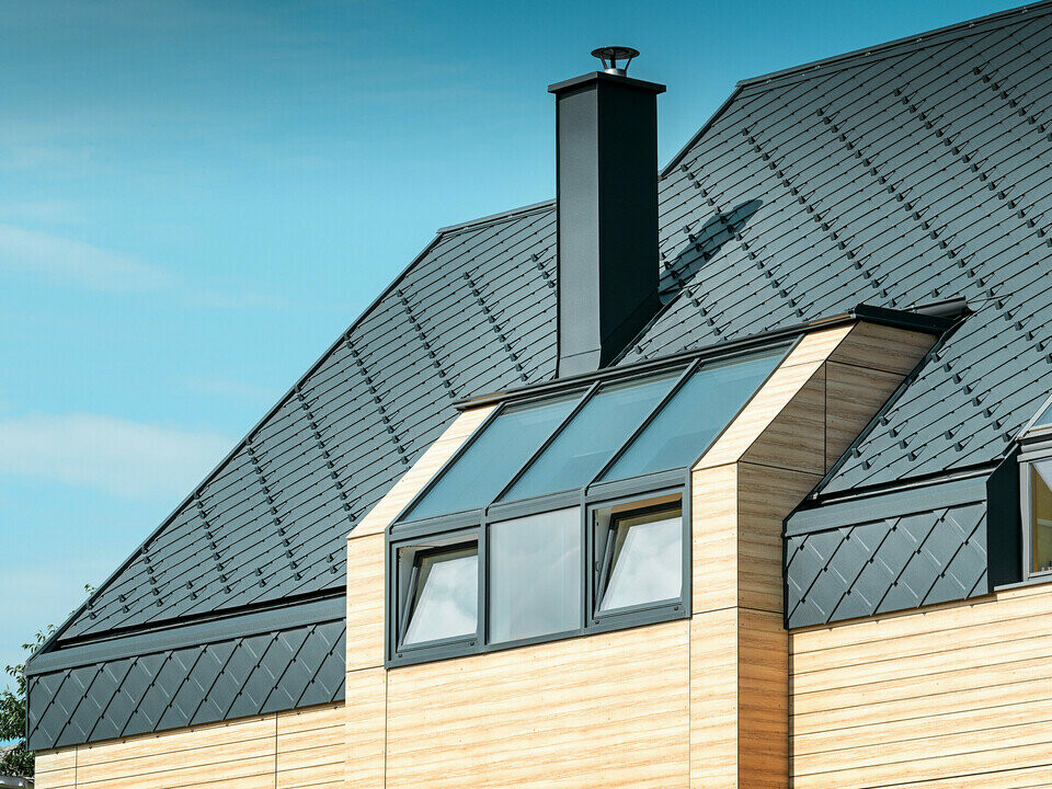 Rodinný dům se sedlovou střechou bez přístřešku s fasádou v dřevěném vzhledu a hliníkovou střechou v antracitové barvě.