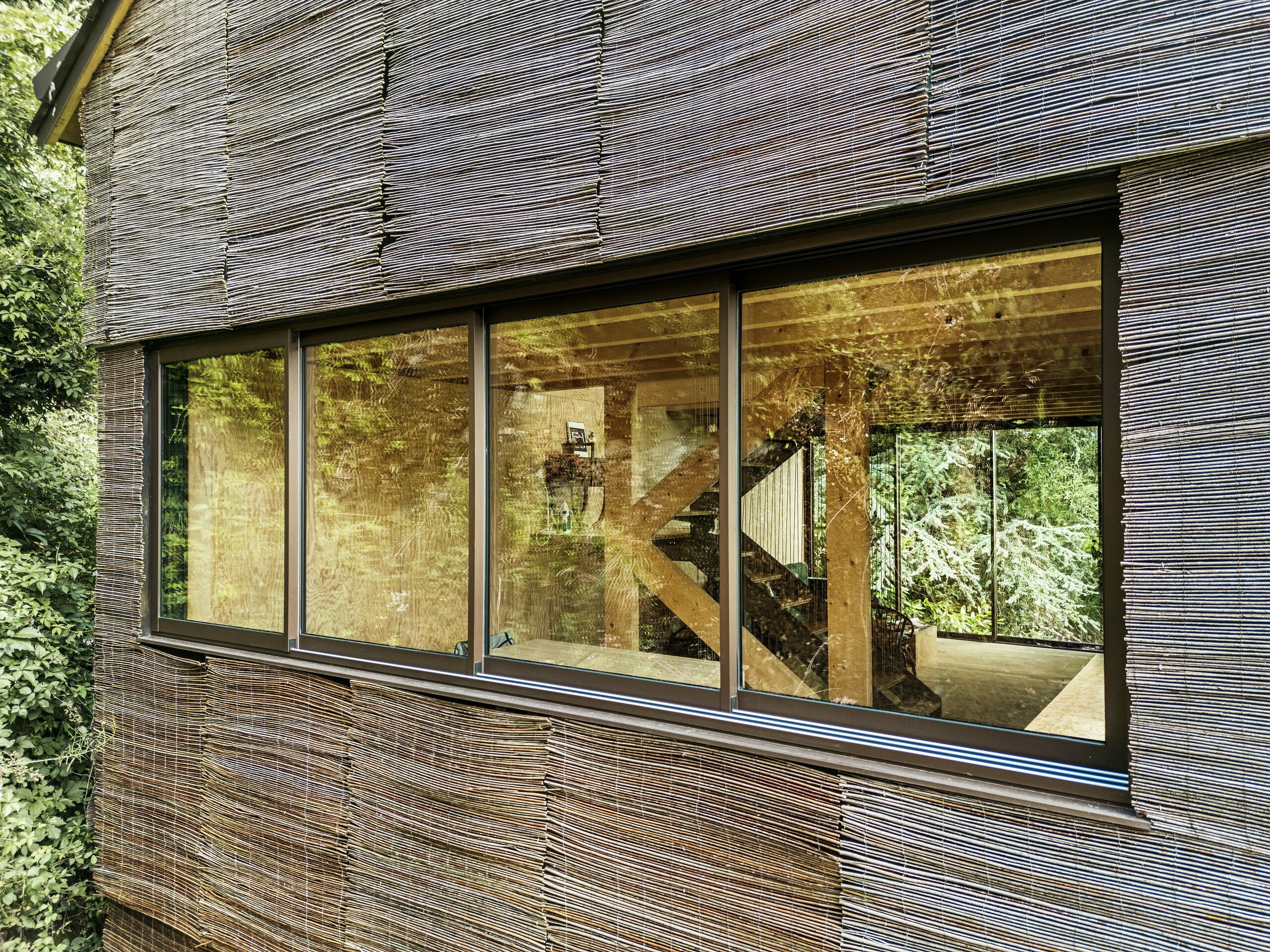 Detail okna s moderním hliníkovým rámem a proutěnou fasádou na domě ve Francii – udržitelný design s falcovanými šindeli PREFA a přírodním prostředím.