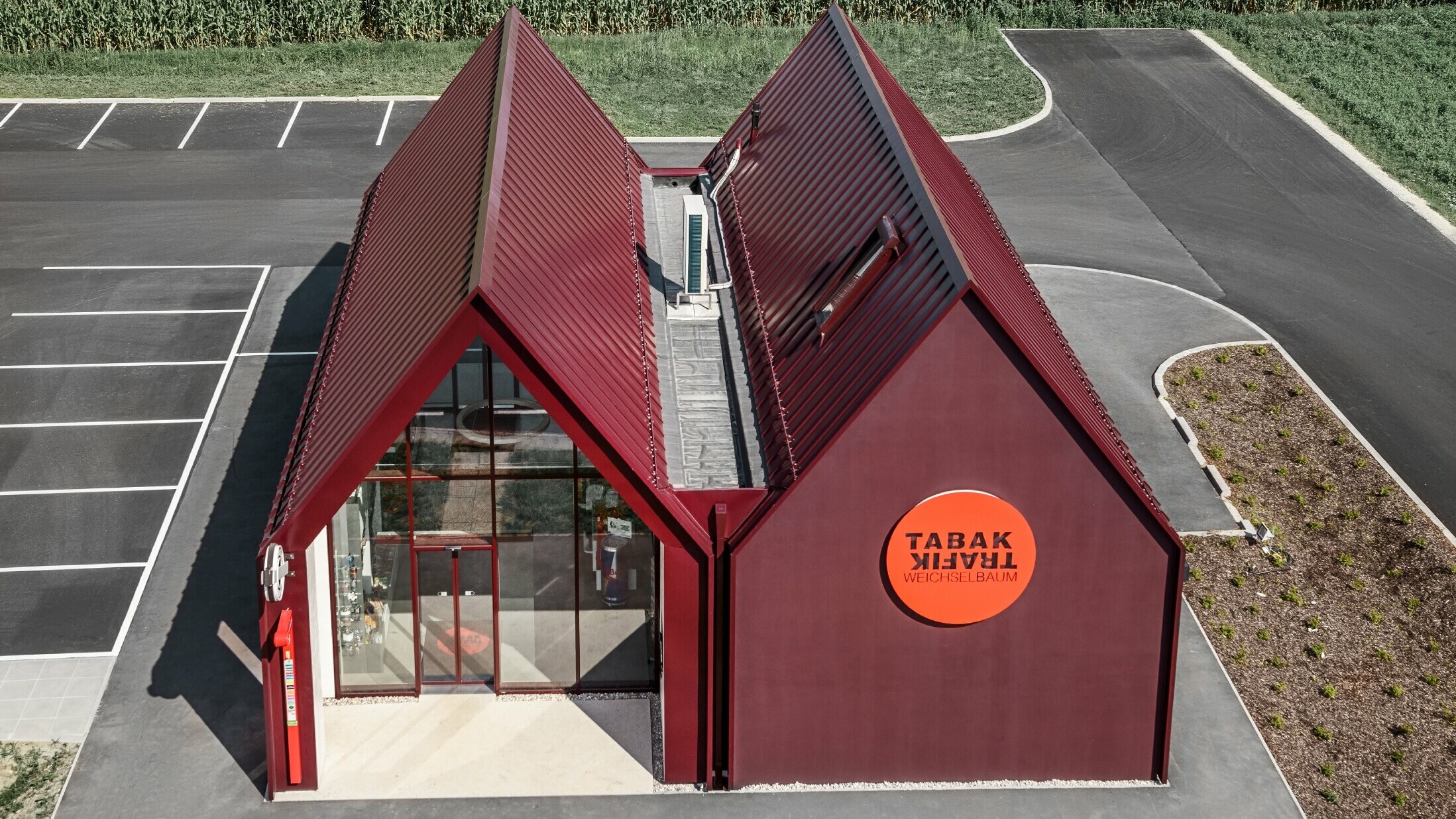 [Translate to Český:] moderne Trafik mit Satteldach und ohne Dachvorsprung und einer Aluminiumhülle von PREFA als Stehfalz- und Winkelstehfalz in der Sonderfarbe schwarzrot ausgeführt